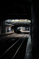shows a commuter line train passing through the platform hallway of BNI city station, which is quite dark during the day. The train is white with red accents, and the platform is empty photo