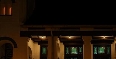 Night view of a building entrance with illuminated stained glass windows and warm lights, creating a serene and inviting ambiance. photo