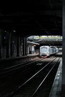 shows a commuter line train passing through the platform hallway of BNI city station, which is quite dark during the day. The train is white with red accents, and the platform is empty photo