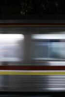 A blurry image of a speeding commuter line train at night, captured with long exposure. The lines of light create a dynamic and abstract composition, highlighting the speed and movement of the train. photo