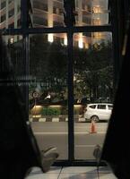 street at night, seen through a window. A white car is parked on the street, and a traffic cone is in the foreground. The scene is quiet and peaceful, with a sense of stillness. photo