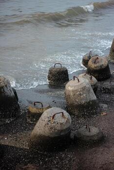 The image focuses on a cluster of concrete breakwaters, partially submerged in the water. The waves are crashing against the breakwaters, highlighting the rugged texture of the concrete. photo