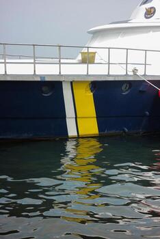 Vibrant nautical scene with a ship's hull reflected on the rippling water, creating an abstract interplay of colors and textures. The image captures the dynamic nature of maritime environments. photo