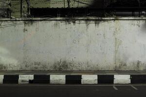 concrete wall with a black and white curb in front of it. The wall is weathered and cracked, and there is a barbed wire fence on top of it. The scene is dark and desolate photo