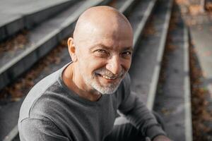 Elderly man sitting on steps, smiling up at camera, autumn leaves scattered around photo