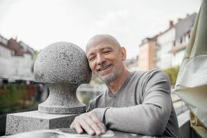Elderly man with a content smile leaning on a stone sphere in a scenic urban park photo