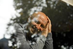 Happy senior man with a beard hugging himself and smiling through a window photo