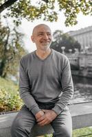 Elderly man sitting on a bench near a river, smiling and enjoying the day photo