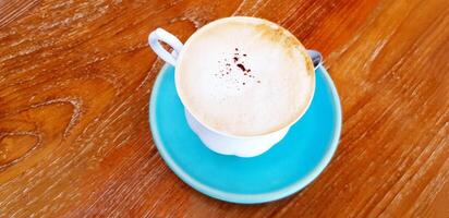 Cup of hot latte coffee with blue bottom plate on wooden table or background with copy space. Refreshment drink, Object, Cafe and Relaxing time concept. photo