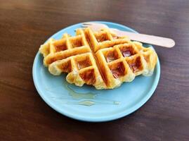 Waffle topped with honey sauce on blue plate at cafe. Flat lay of Sweet bakery on dish with copy space. Snack on table. photo