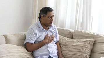 A middleaged Indian man with chest pain sitting on the sofa at home an isolated on white background photo