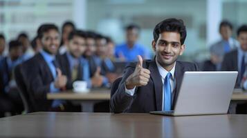 A happy Indian businessman gives a thumbs up while sitting at a table with a laptop photo
