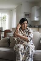 A middleaged Indian woman sitting on the couch and holding her hand in pain with an angry expression photo