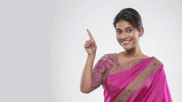 A happy Indian woman in a saree pointing her finger up and looking at the camera on a white background photo