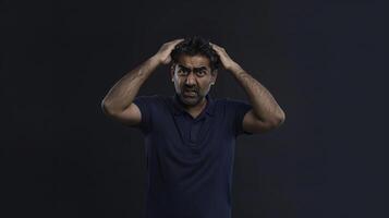 An Indian man hands on head holding hair with a distressed expression looking at the camera photo