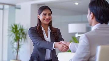 A happy beautiful young Indian businesswoman shaking hands with a client at work standing near the meeting table in the office photo