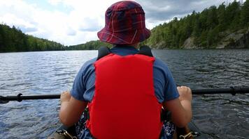 A man from behind, rests with his paddle in a canoe on the water photo
