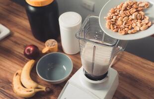 preparation of a protein smoothie by adding a cup of roasted peanuts photo