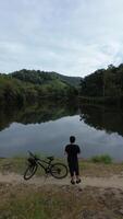 Man Resting with His Bicycle by the Lake, Enjoying the Beautiful Summer Morning Background photo