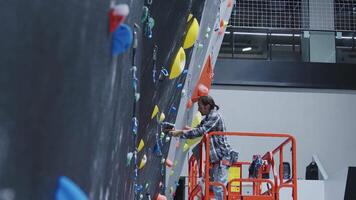Worker installing climbing holds on an indoor climbing wall using a lift, showcasing the setup process in a modern climbing gym video
