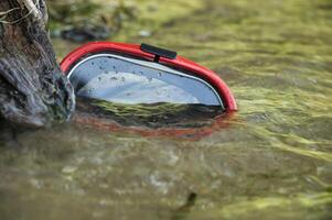Red scuba diving mask partially submerged in shallow water near tree trunk photo