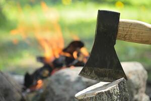 Hatchet embedded in a log of wood opposite campfire photo