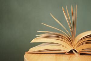 An open book with its pages gently turning rests on a wooden table in the breeze photo