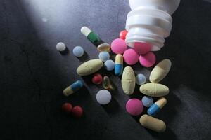 Capsules and pills spilled from a bottle, displaying various medications and supplements photo