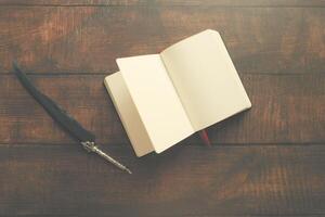 A blank notebook on a wooden table with a quill pen, perfect for creative writing and journaling photo