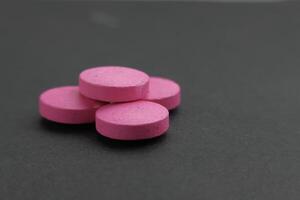 The image shows a detailed view of pink round pills set apart against a dark backdrop photo