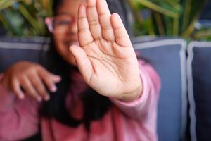 A joyful child is smiling and showing an open palm in a friendly gesture, captured indoors in a casual setting photo