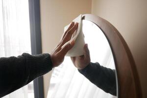 Man Cleaning a home Mirror with a tissue . photo