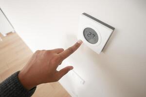 Hand Adjusting Smart Thermostat on White Wall for Optimal Home Temperature Control photo