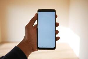 A person holding a smartphone with a blank screen in a welllit room, showing modern digital usage photo