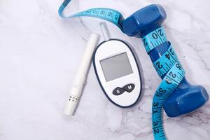 Top view glucose meter machine and dumbbell on white photo