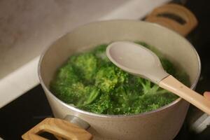 Boiling broccoli in a pot with a wooden spoon on the stove, preparing a healthy meal photo