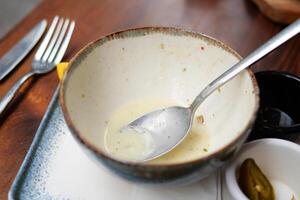 An empty dirty bowl with a spoon on a table . photo