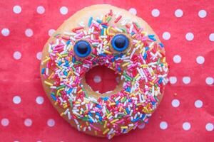 Funny smiling face donut with sprinkles on red background. photo