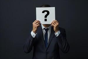 a man in a black business suit hides his face behind a white sheet of paper with a question mark photo