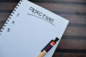 Concept of Objectives write on book. Supported by an additional services isolated on wooden table photo