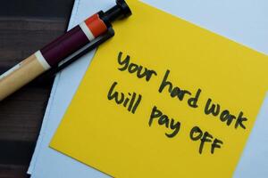Concept of Your Hard Work Will Pay Off write on sticky notes isolated on Wooden Table. photo