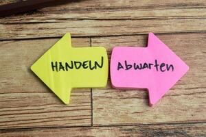 Concept of Learning language - German. Haldeln or Abwarten it means Hold on or wait written on sticky notes. German language isolated on Wooden Table. photo