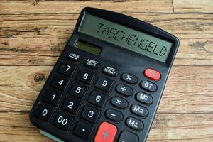 Concept of Learning language - German. Taschengeld it means pocket money written on Calculator. German language isolated on Wooden Table. photo