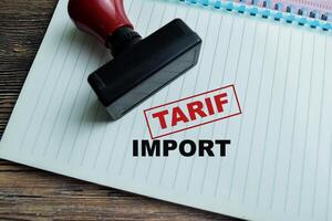 Red Handle Rubber Stamper and Tarif Import text above book isolated on wooden background photo