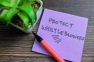 Concept of Protect Whistleblowers write on sticky notes isolated on Wooden Table. photo