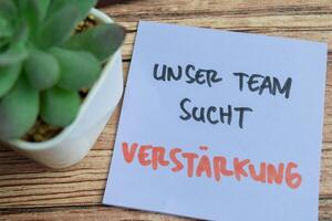 Concept of Learning language - German. Unser Team Sucht Vestarkung it means Our team is looking for reinforcements written on sticky notes. German language isolated on Wooden Table. photo