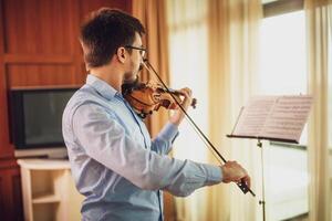 Man playing violin at home. He is practicing for live performance. photo