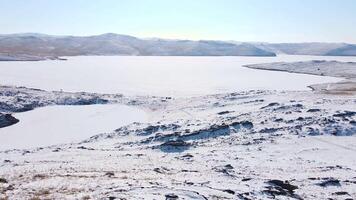 Embark on an adventurous winter hiking journey near a frozen lake amidst a mountainous scenery video