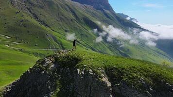 A hiker is navigating along a winding road on a mountain, surrounded by lush green landscape video