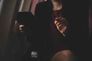 Blonde female tourist checking incoming notification on smartphone sitting on seat of airplane with netbook.Young businesswoman share media from telephone on laptop computer during plane flight photo
